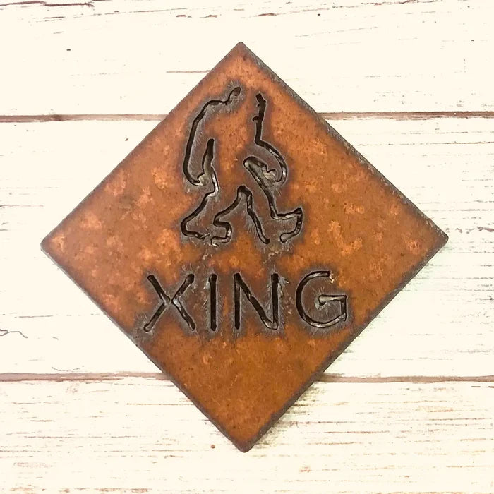 Rusty diamond shaped magnet with a Bigfoot silhouette and the word XING