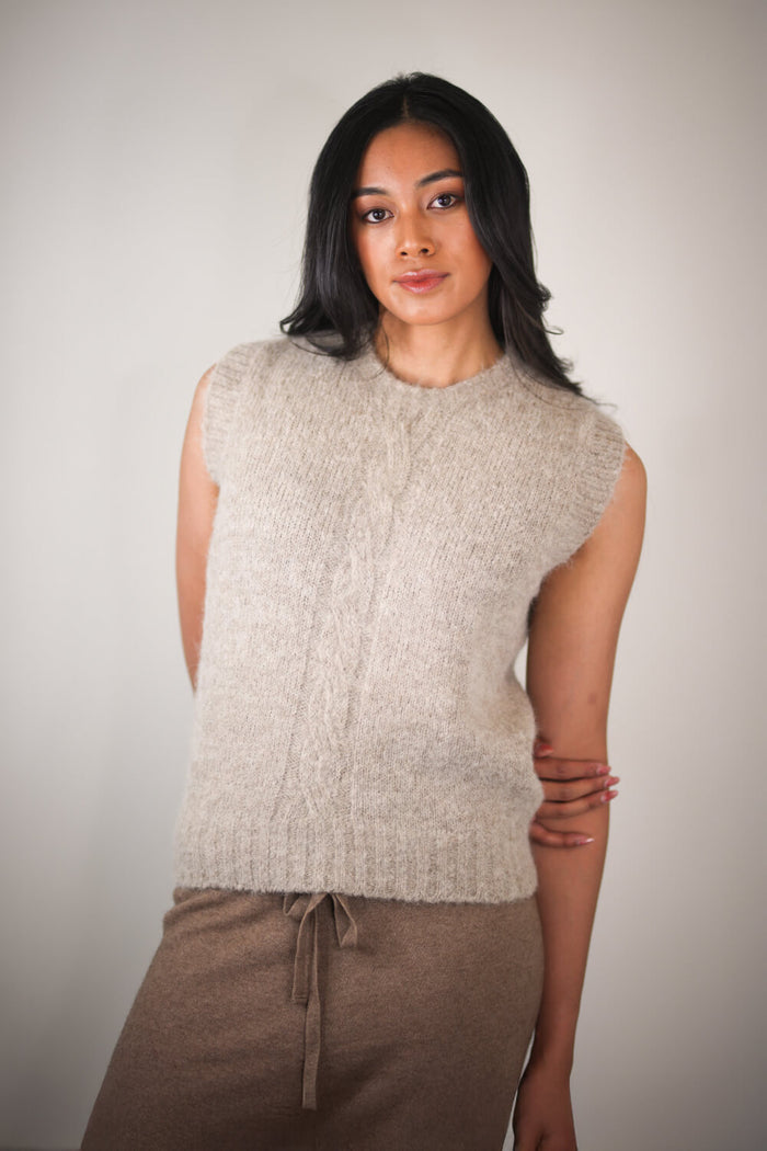 Woman wearing a beige knitted sleeveless sweater against a plain background