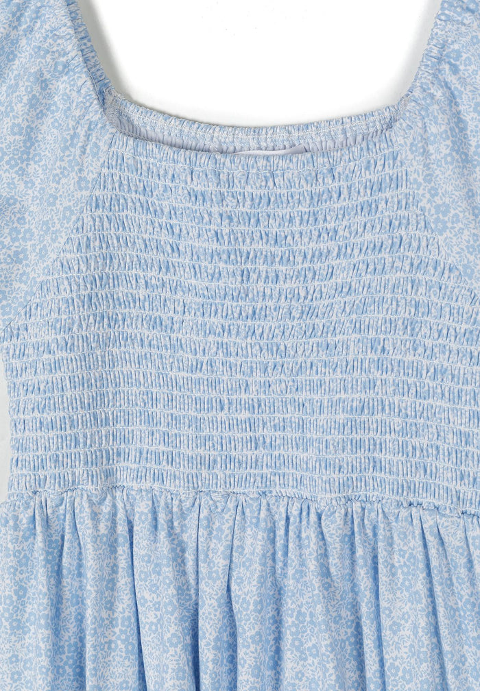 Detail of a girls light blue floral summer dress with gathered shearing and square neckline.