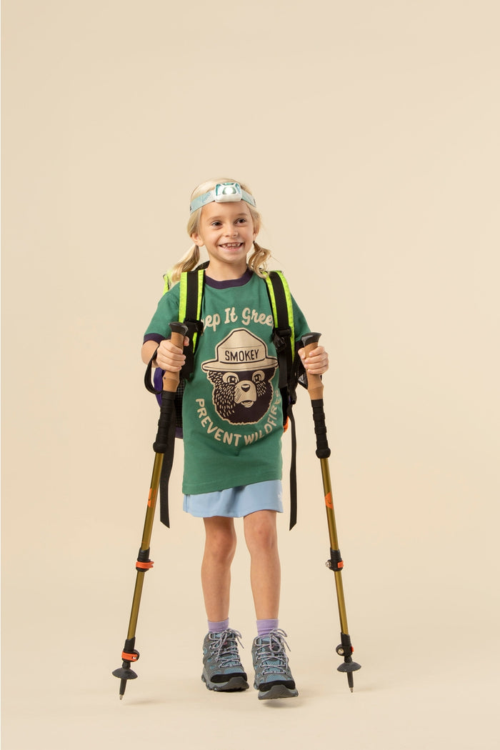 Young girl wearing the Keep It Green Kids' Ringer Tee with Smokey Bear graphic, hiking backpack and trekking poles.