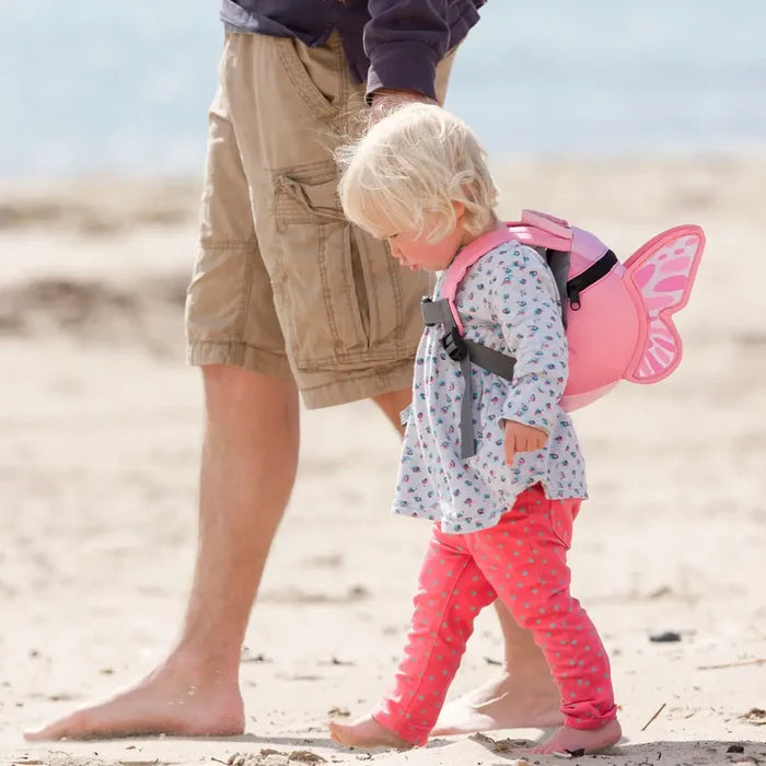 Little girl walking along the beach holding an adults hand whilst wearing a Littlelife Butterfly Toddler Backpack