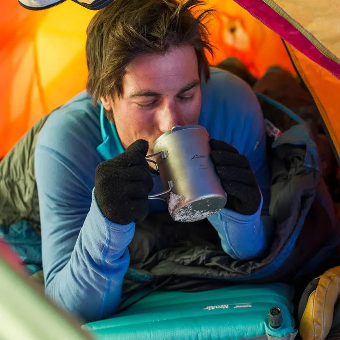 Lifestyle shot of a male wearing sub zero factor 2 thermal mid layers drinking a hot drink whilst inside a tent inside his sleeping bag that also has a Sub Zero Meraklon sleeping bag liner