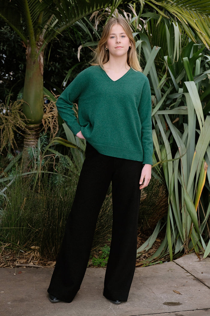 A woman standing outside wearing black merino active pants and a green sweater.