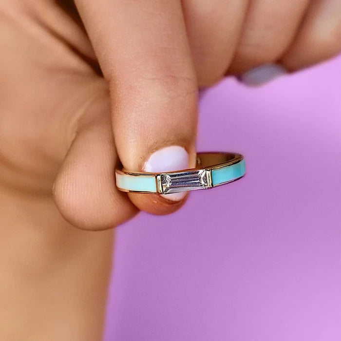 Gold two tone ring with white and turquoise enamel inlays and a central baguette diamond held between fingers