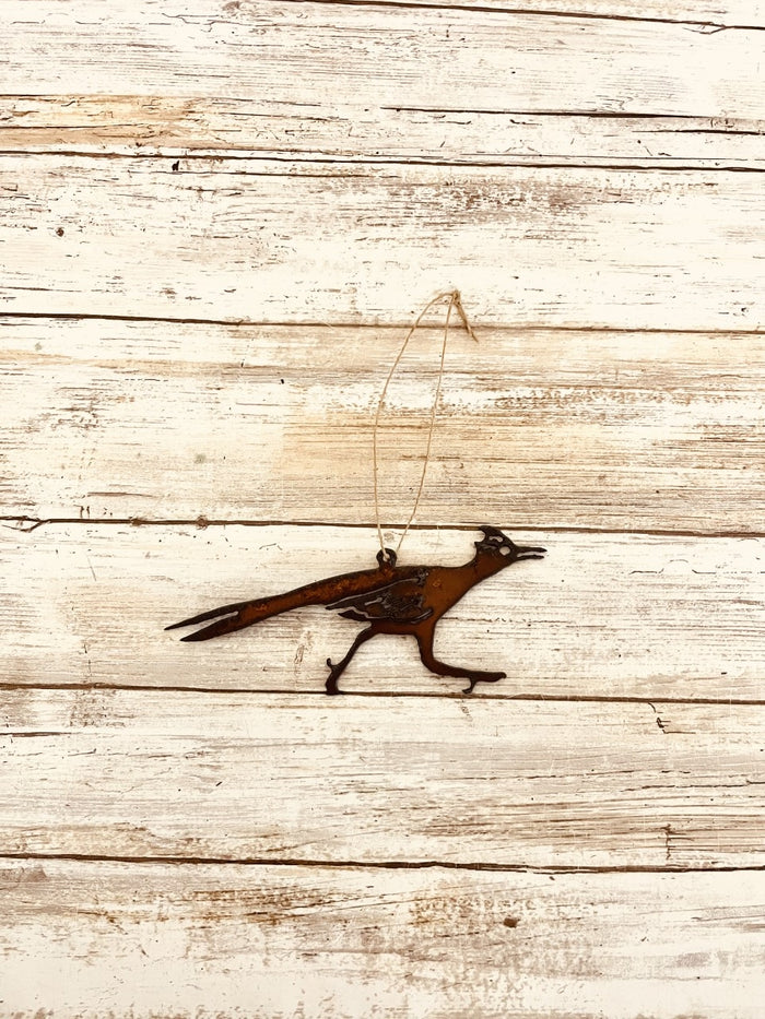 Rusty metal road runner ornament with long beak hanging from twine against rustic wood