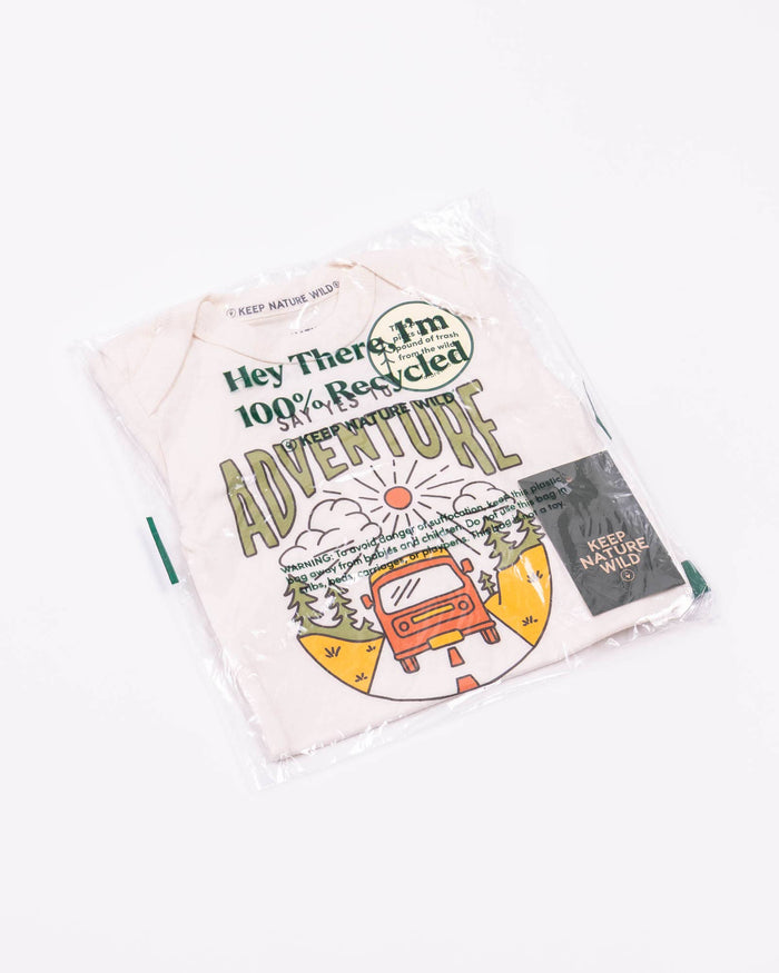 Cream baby onesie in plastic packaging displaying the adventure design visible through the bag