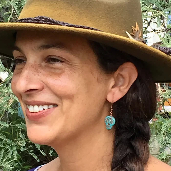 Turquoise sugar skull dangle earrings worn by a woman in a tan hat.