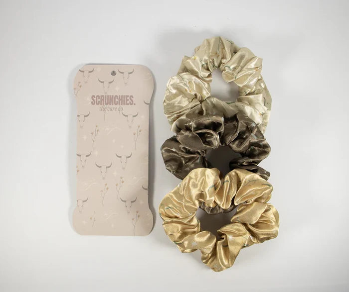 Three satin scrunchies in cream brown and gold beside a cream Western print packaging.