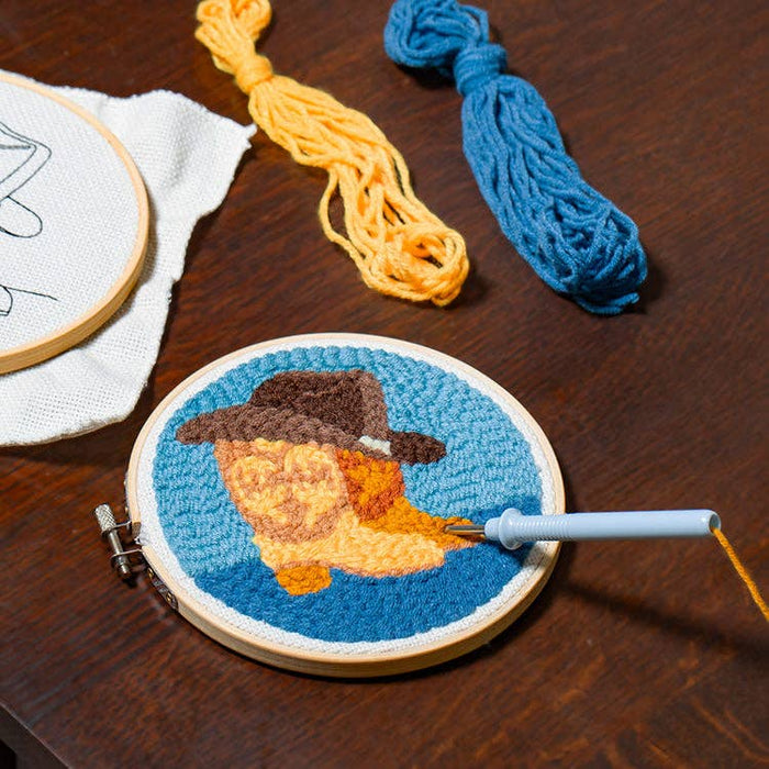 Western Punch Needle kit showing a round hoop with a cowboy portrait and bright yellow and blue yarn skeins.