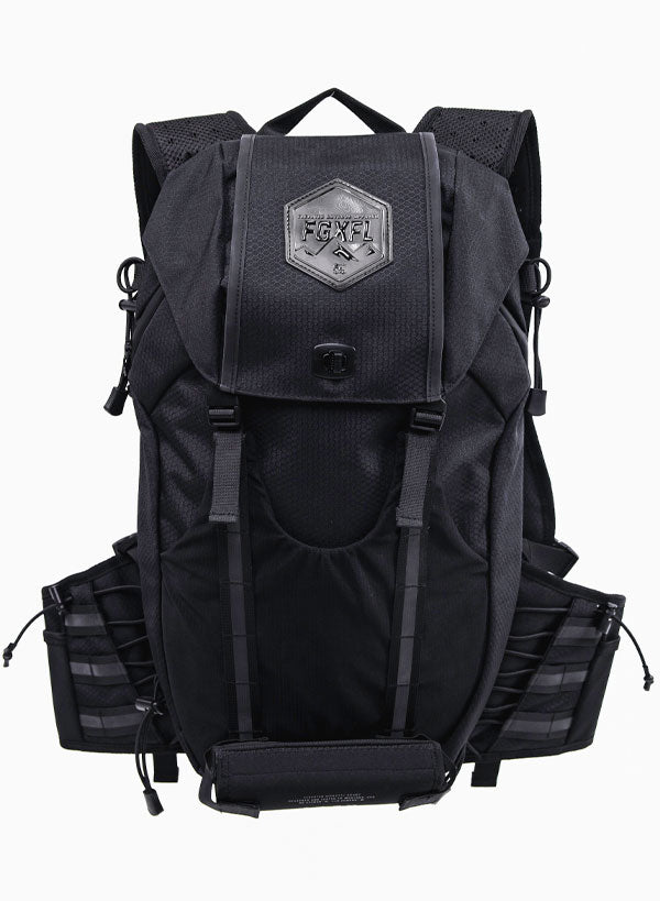 The back of our Apex bag black in color. The top flap of the bag has a  hexagonal patch. The patch reads "ELEVATED OUTDOOR APPAREL" FGXFL above a range of mountains. The top flap has two buckles to buckle to the body of the pack.