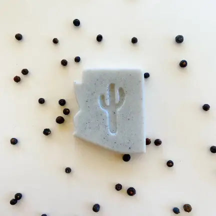 Arizona Juniper Soap bar with scattered peppercorns on a white surface.
