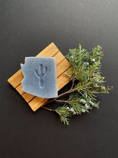 Blue grey Arizona Juniper Soap resting on a wooden slat board with juniper sprigs.