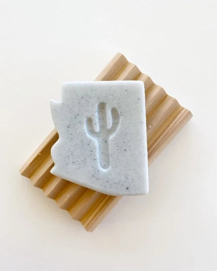 Arizona Juniper Soap bar with a cactus silhouette embossed on a speckled light gray block resting on a wood ribbed board.