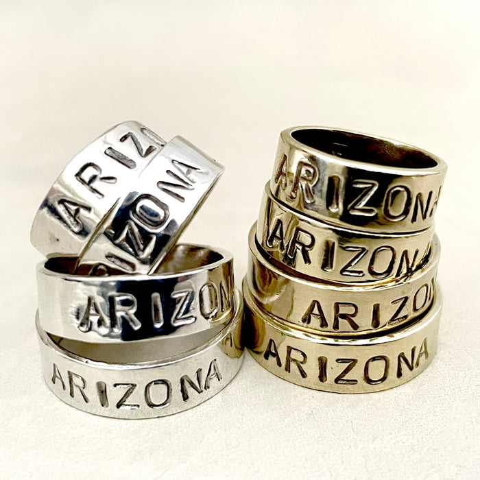 Stack of silver rings engraved with ARIZONA around the bands