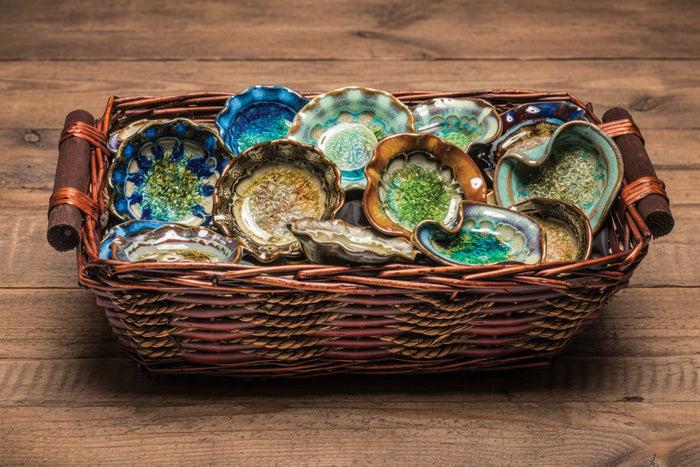 Assorted ceramic trinket dishes in blue and green glazes arranged in a woven basket.