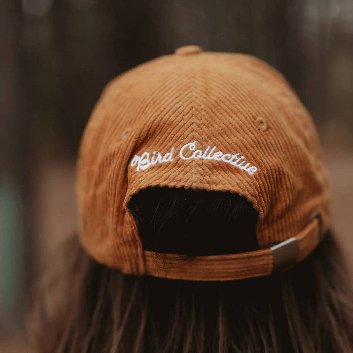 Back view of mustard corduroy hat worn by a person with white embroidery on the back