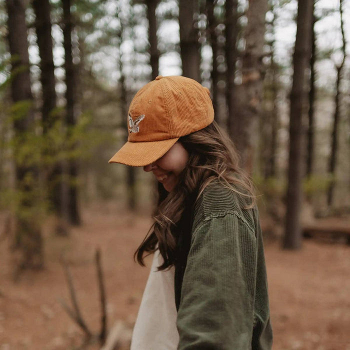 Profile of a person wearing the mustard corduroy Barn Owl hat in a forest setting