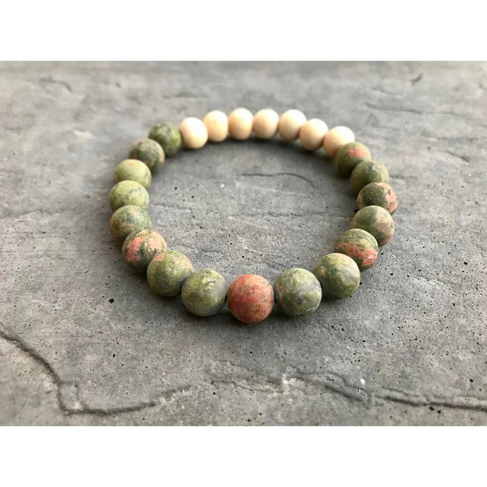 Unakite Stone Aromatherapy Bracelet worn on the wrist beside other beaded bracelets on a gray surface.