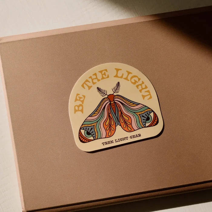 Be The Light sticker with a colorful moth artwork applied to a laptop.