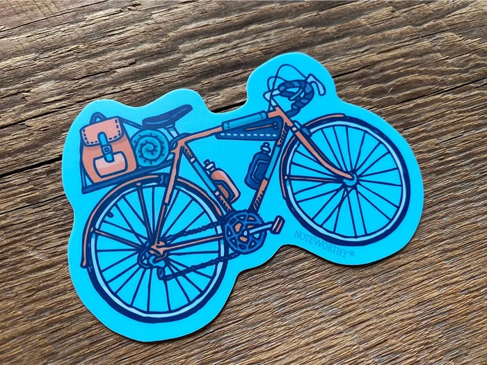Blue bicycle sticker with brown pannier bag and gear on a wooden surface