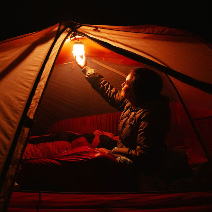 Lifestyle image of a woman in a tent at night using a Biolite AlpenGlow LED lantern attached to the  ceiling to provide light