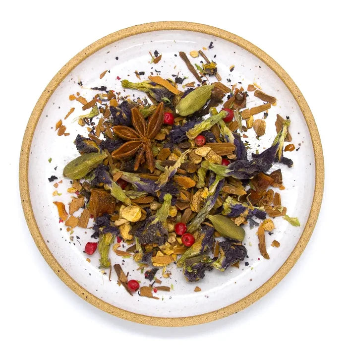 Loose Blue Chai Herbal Tea blend with dried flowers, spices including star anise, on a round white plate with cork rim.