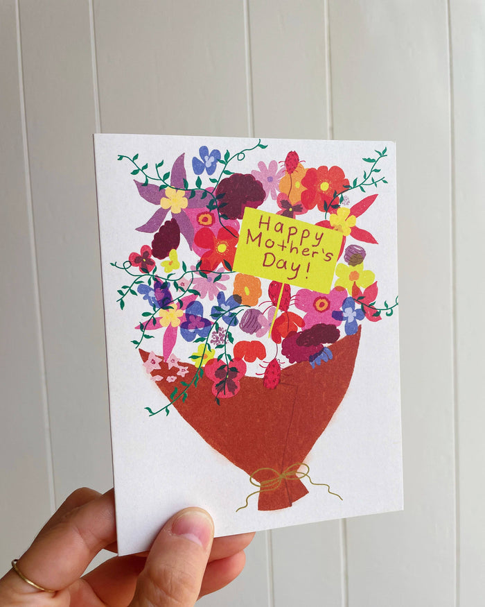 Person holding a colorful bouquet Mother's Day card against a pale paneled wall