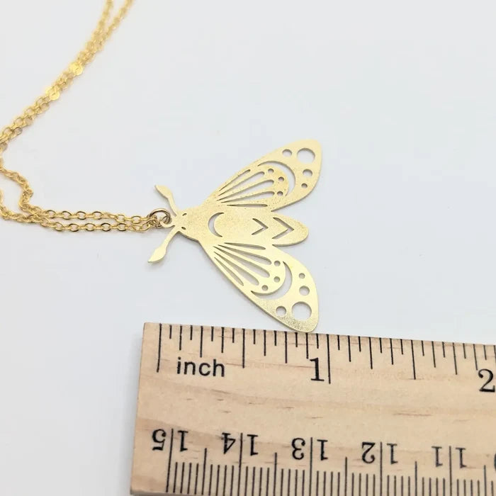 Close up of a gold brass moth pendant on a chain with a ruler showing scale