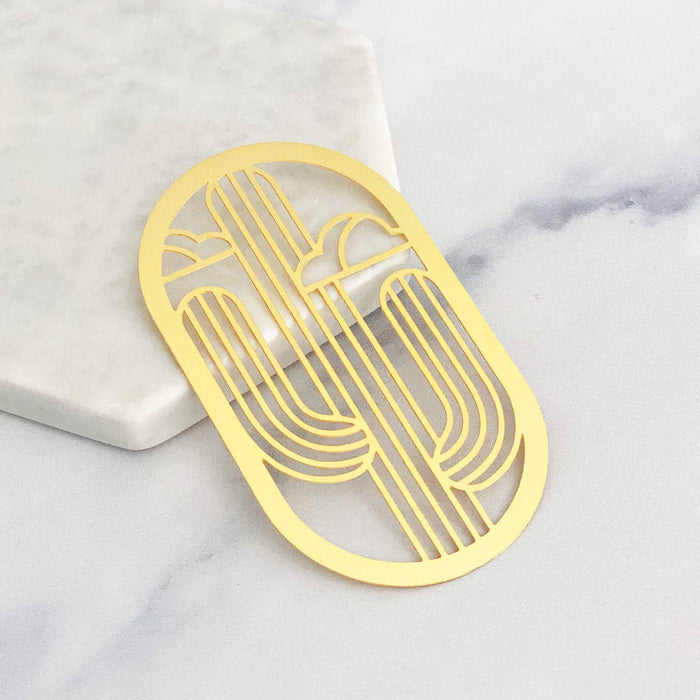 Yellow brass bookmark with a cutout saguaro cactus design on a white marble surface