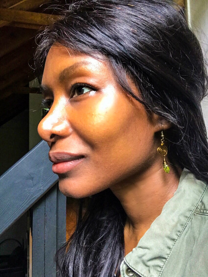 Side view of a woman wearing brass spiral olive leaf earrings with green teardrop charms