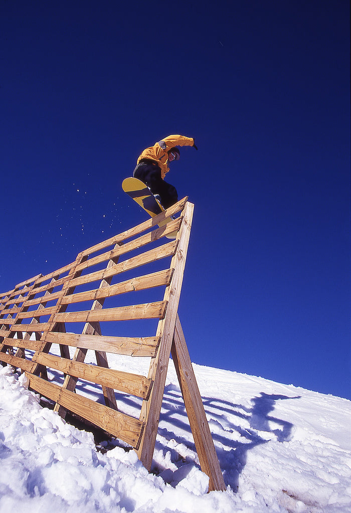 Jason Brown doing a boardslide on top of a tall wind fence on a snowy slope [Variant: True Black]