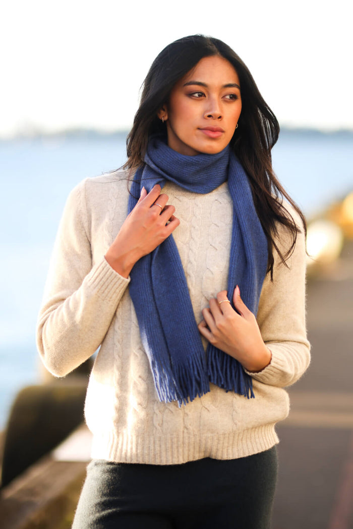 Woman wearing a blue scarf and beige sweater by a waterfront