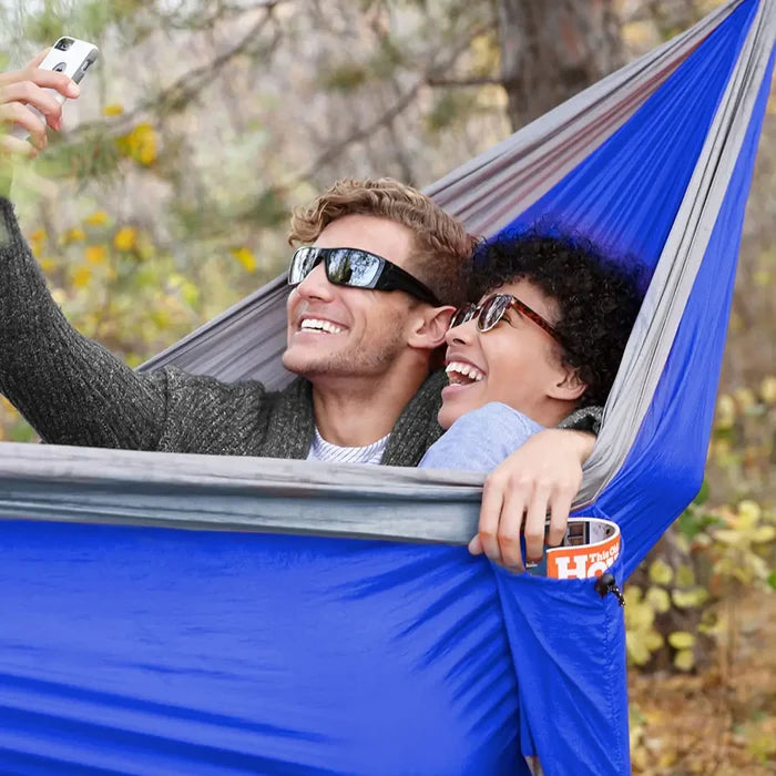 Coghlans double parachute hammock in grey/blue set-up with two people lying in it in a forest