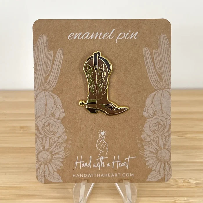 Cowboy boot enamel pin with a gold outline mounted on a brown packaging card.
