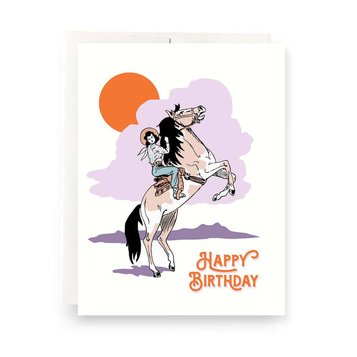 Cowgirl birthday greeting card with a rider on a rearing horse against a sunset and purple clouds.