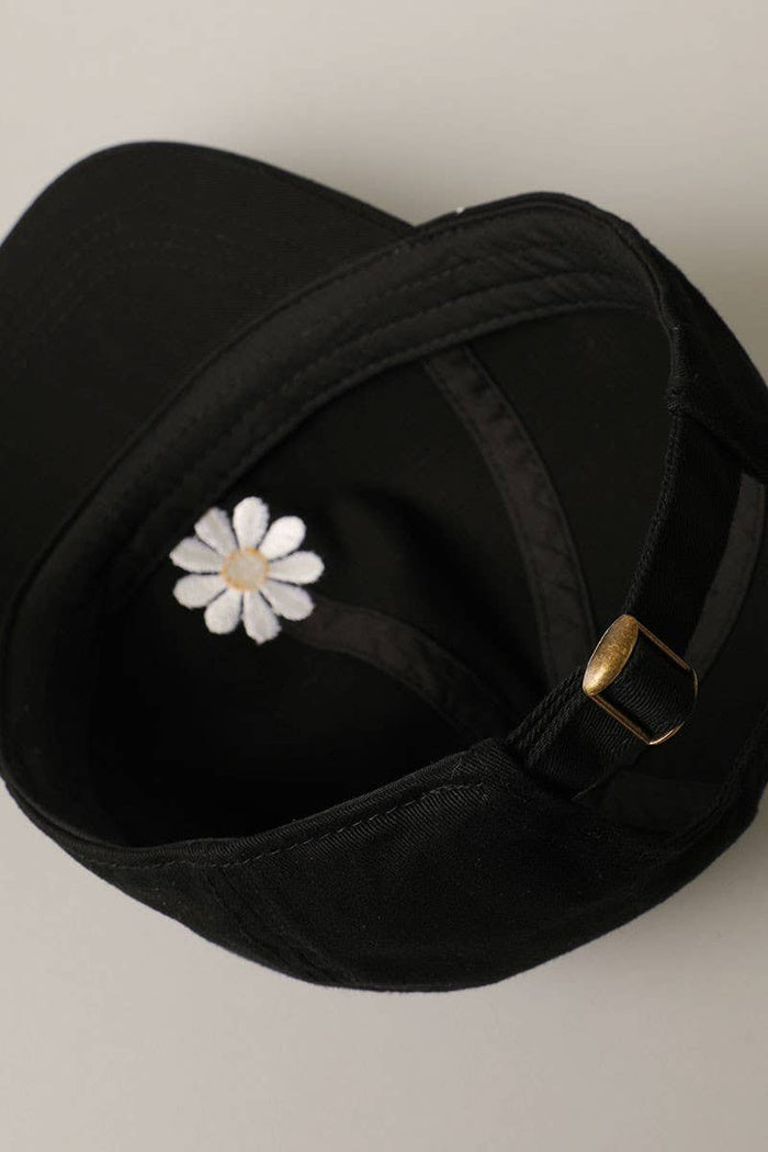 Inside view of black cap showing a white daisy embroidery near the crown and a brass buckle on the back strap