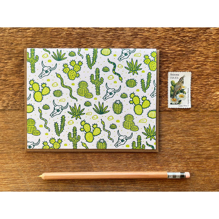Desert Cactus Card with bright green cacti on white background, shown on a wood surface with a pencil.