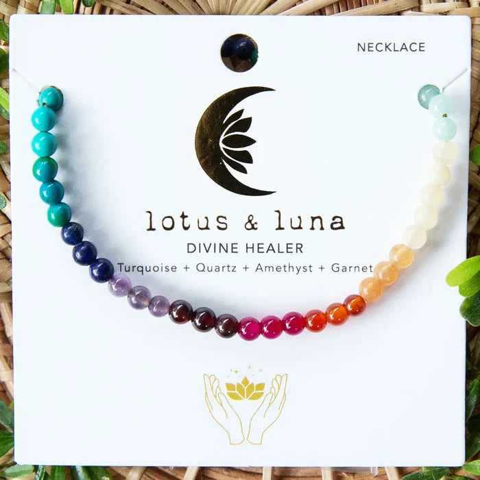 Rainbow beaded necklace laid across a white display card with Lotus Luna branding on a wicker background.