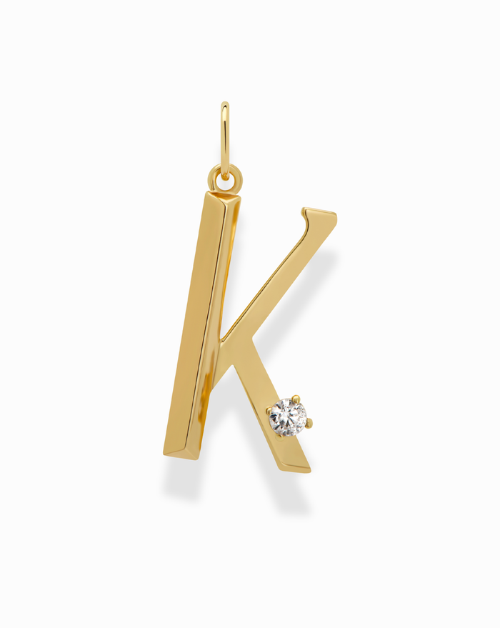 The Eloise Letter Charm by Mod + Jo is a gold necklace with a K-shaped pendant, featuring a small round cubic zirconia on the lower right leg, shown against a plain white background.