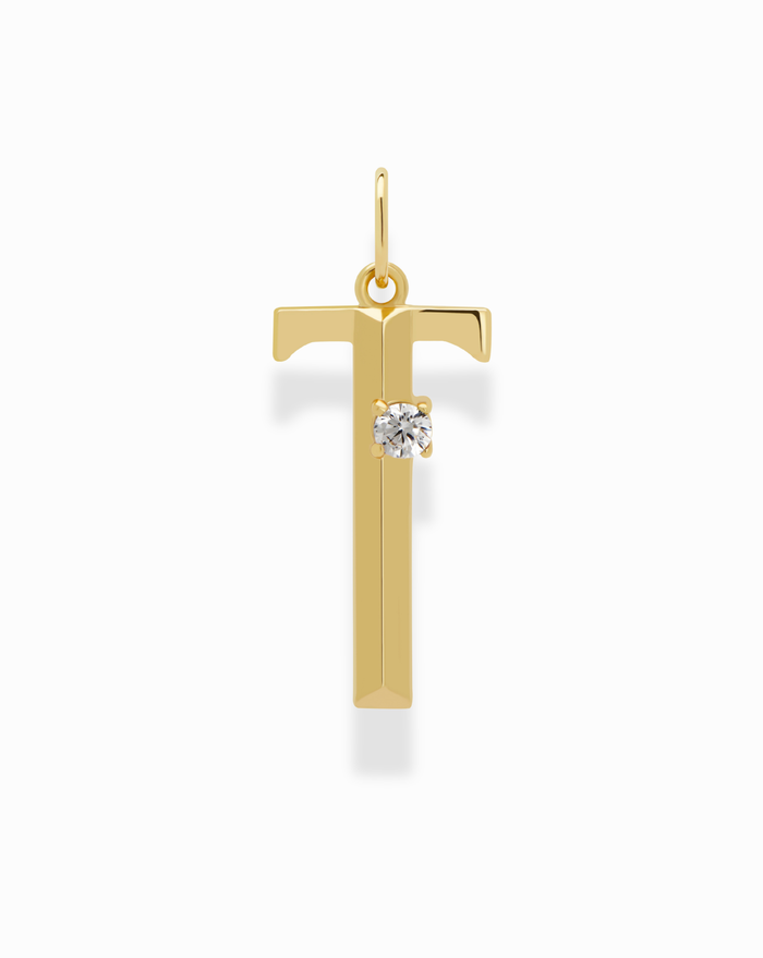 The Eloise Letter Charm by Mod + Jo is a gold T-shaped initial featuring a small round cubic zirconia on the left of the crossbar, shown against a white background.