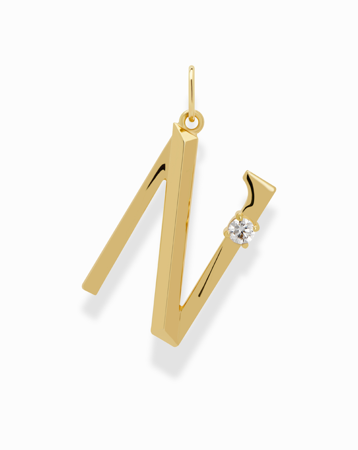 The Eloise Letter Charm by Mod + Jo is a gold necklace featuring an "N"-shaped pendant with a small round cubic zirconia on the right, displayed against a white background.