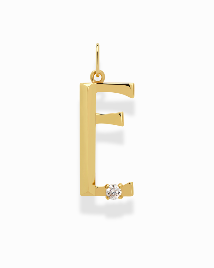 The Eloise Letter Charm by Mod + Jo is an E-shaped gold pendant with a sparkling cubic zirconia at the bottom right, shown on a white background.