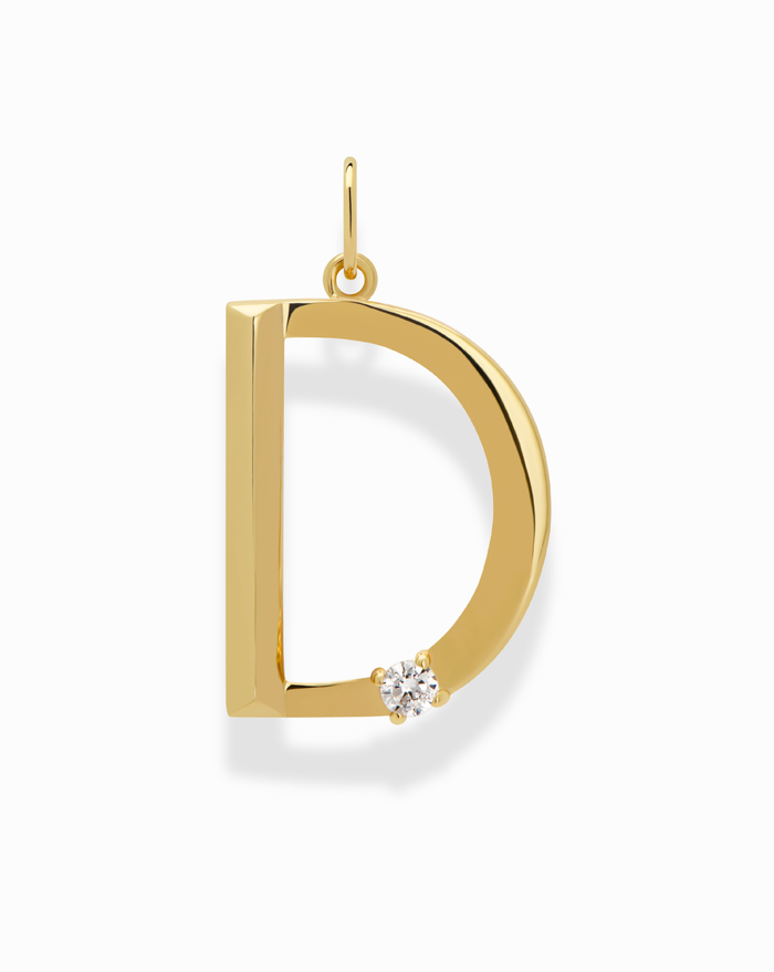 The Eloise Letter Charm by Mod + Jo is a gold initial necklace shaped like a "D," with a sparkling cubic zirconia at the curve’s base, shown against a plain white background.