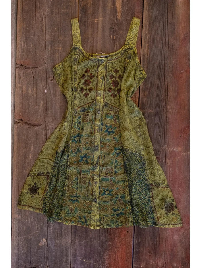 Embroidered patchwork mini dress in olive green with floral motifs displayed against a rustic wooden backdrop.