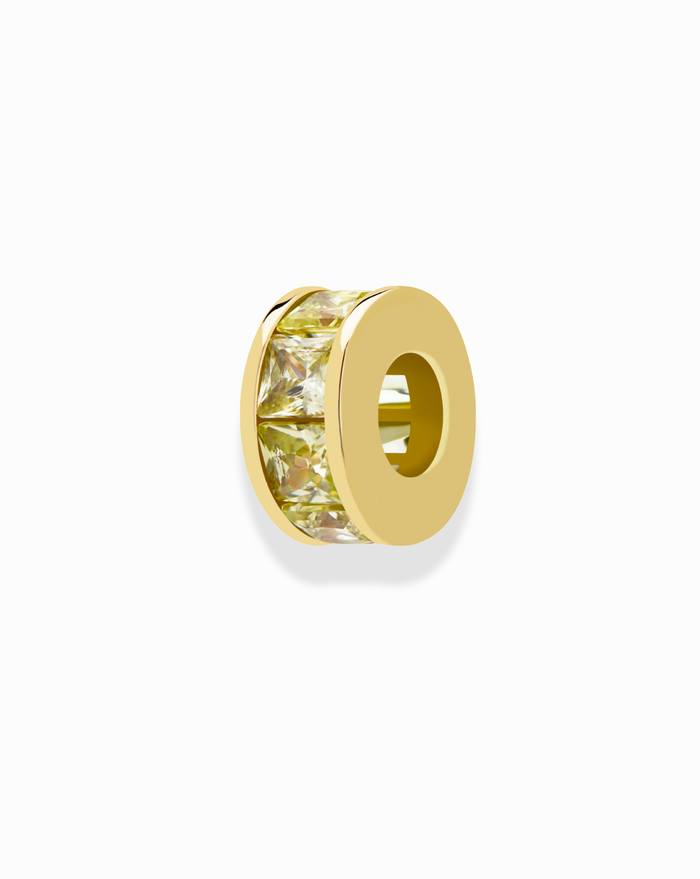 The Mod + Jo Este Birthstone Charm Spacer is a round gold bead with a hollow center and a band of yellow, princess-cut gemstones—ideal for personalized jewelry. Shown on a white background.