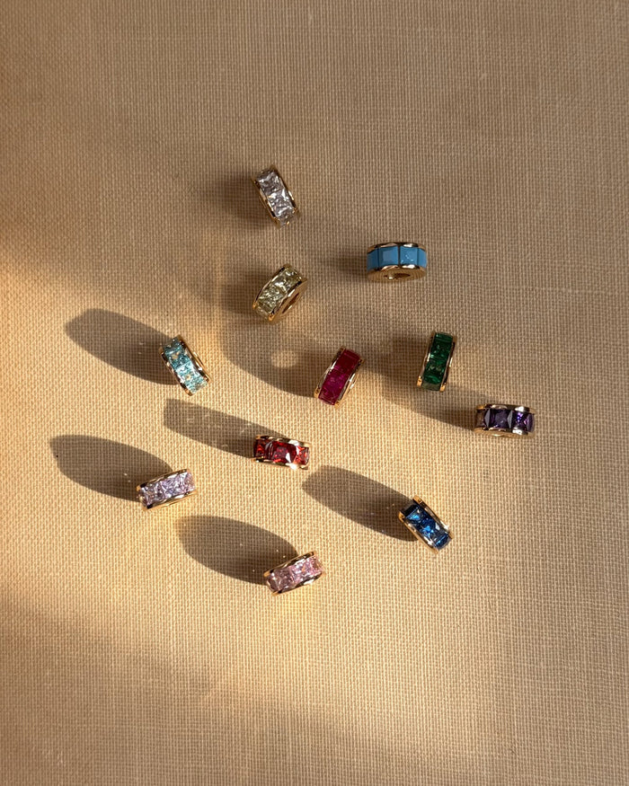 The Este Birthstone Charm Spacer by Mod + Jo features gold rings with vibrant blue, green, pink, purple, red, and yellow gemstones. Use as a personalized charm or necklace spacer to add colorful birthstone style to your jewelry.