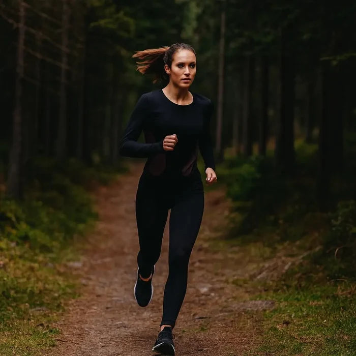 Woman running on a path in a forest wearing a Sub Zero Factor 1 Plus Womens Long Sleeve Base Layer Stretch Top Pink Black with black leggings