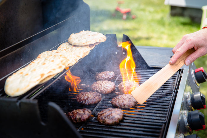 Flatbreads grilling on a barbecue with a wooden spatula flipping them