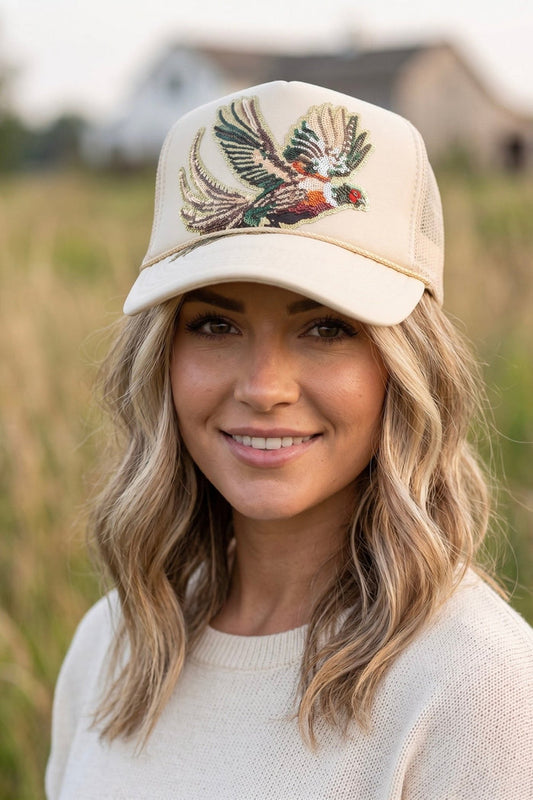 Cream premium foam trucker hat featuring a large multicolor sequin pheasant patch, breathable mesh back, and adjustable snapback closure.