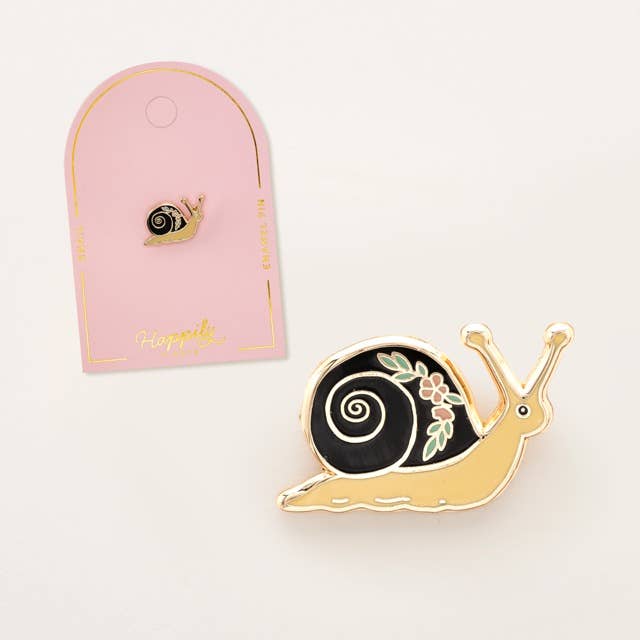 Small snail enamel pin on a pink display card with a larger snail pin nearby.